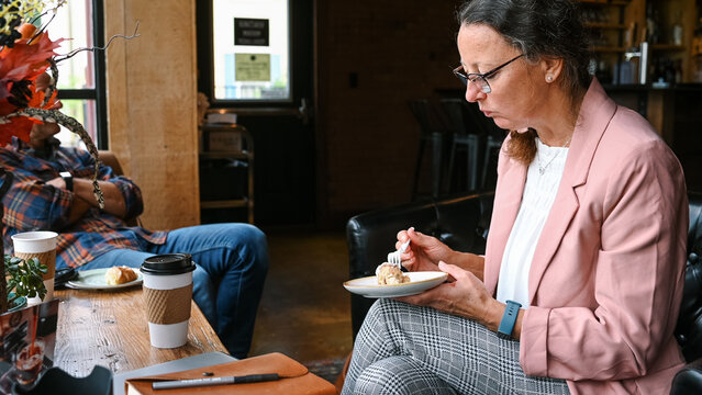 woman in business attire eating pastry at coffee shop