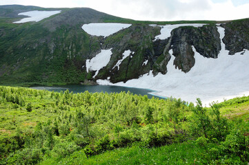 Obraz premium A picturesque lake with turquoise water at the foot of a high cliff with the remains of snow on the slopes.