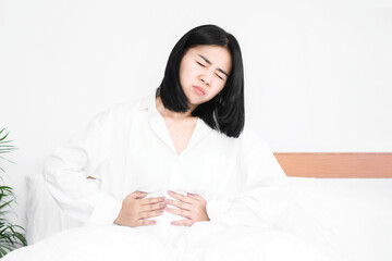 Asian woman suffering from stomach ache,  sitting in bed