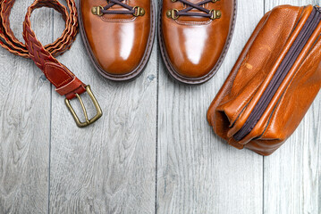 Brown leather men's accessories. Boots, belt and nessesor on a gray, wooden background