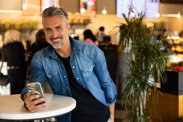 Cheerful senior man using smartphone in cafe