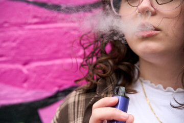 Young woman blows smoke after inhaling from vape pen