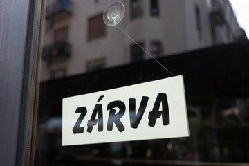 Sign in the shop window behind a pane of glass saying 'zárva' which means 'closed'. the shop is closed. end of business. closure of business. modern font.