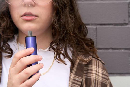 Young woman standing in street using vape pen
