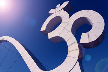 A fragment of a bridge in Haridwar with a giant Om symbol against a blue sky with a sun glare.