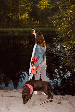 Young Woman While Walking With A Dog Makes Photos On The Smartphone. 