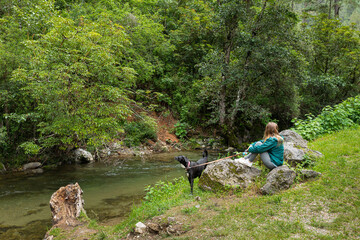 woman sitting on a large rock with her dog in front of a river