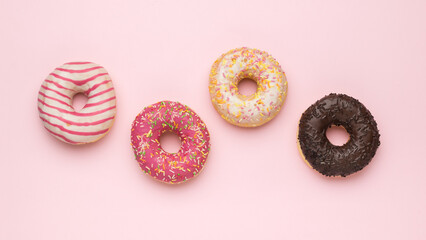Four multicolored glazed donuts on a pink background. The minimal concept of popular baking.