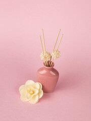 A large white flower and a pink vase with incense sticks on a pink background.