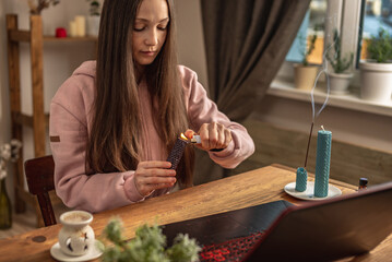 Woman is sitting in front of a laptop, lighting an aroma stick for creating an atmosphere for meditation and relaxation. Concept of a remote therapy and meditation session
