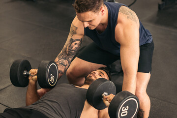 Man training dumbbell bench press in gym with spotter