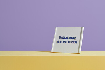 Welcome we're open sign on table over purple