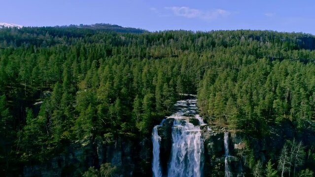 Drone revealing beautiful and majestic landscape covered with pine trees and Tvinnefossen waterfall flowing through it near Voss, Norway