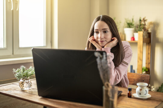 Woman is sitting in front of a computer screen in a calm pleasant atmosphere and attentively listens to video training or an online session or just communicates with a friend