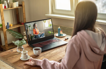 Woman is sitting at a table in front of a laptop, meditating and relaxing while listening to an instructor online or a video lecture. Concept of a remote therapy and meditation session