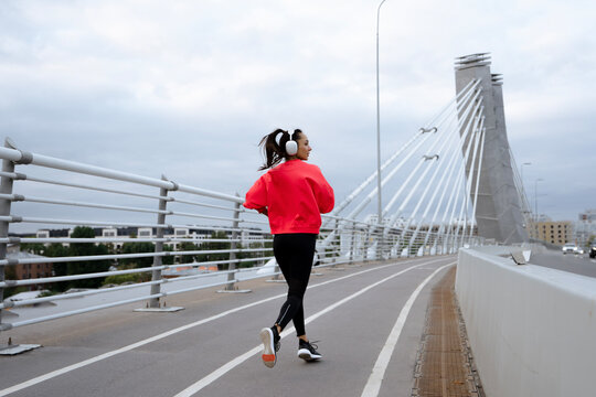 view of young woman runner with earphones jogging in city.
