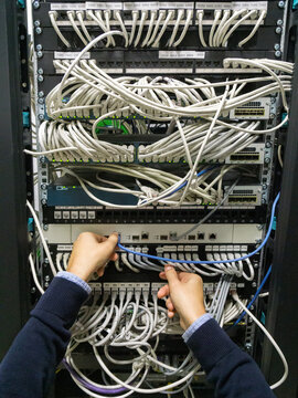 Hands of an IT technician man connecting cables in a rack