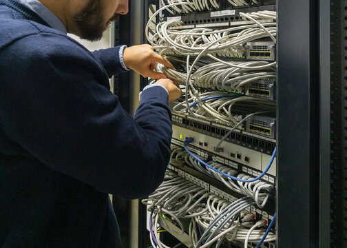 It technician man connecting cables in a communications rack
