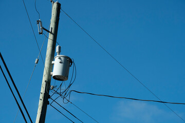 An image of a power transformer and power lines against a bright blue sky. 