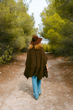 back of girl with hat and brown poncho walking in the woods 