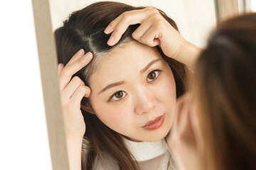 Fototapeta premium 鏡で頭皮を見る女性。