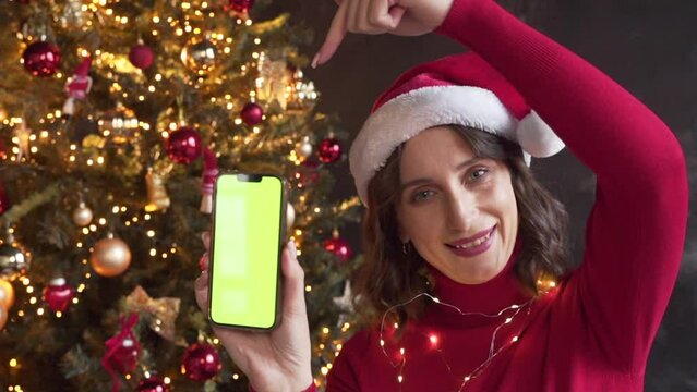 Woman in red sweater and Santa's hat holding a mobile phone with a green screen