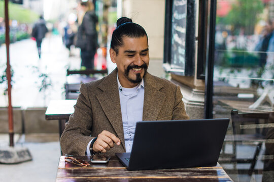 Latino man smiling while working on his computer at cafe