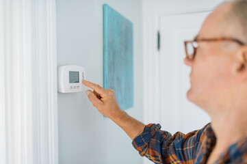 Middle Aged Man with glasses turning down the heater thermostat. 