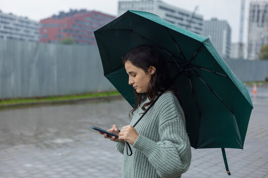 woman stands under an umbrella with a phone