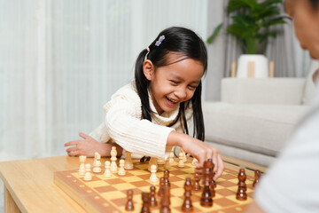 Asian little girl is playing chess board game withe father in the living room with happy moment....