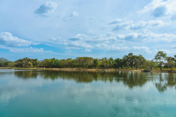 Beautiful and peaceful view of large reservoir with surrounding mountain and trees in beautiful sunshine and cloudy sky in Thailand. Tranquil and beautiful natural scenery landscape of reservoir lake.