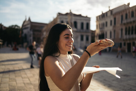 Fototapeta Young woman eating a slice of pizza on the street in Italy