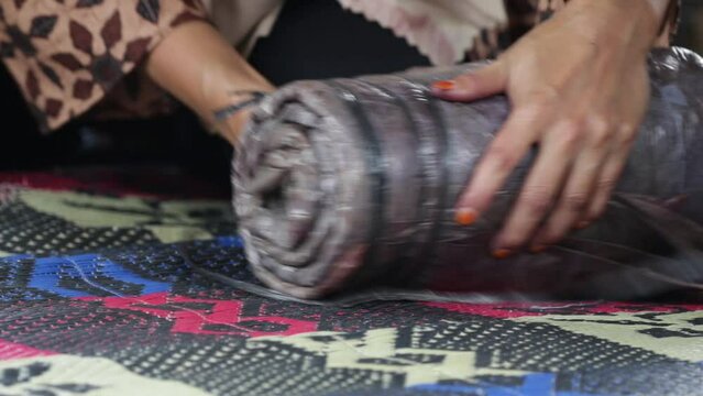 home industry videos. Indonesian women's hands folding a roll of cloth covered in plastic during the process of folding an ecoprint batik cloth.