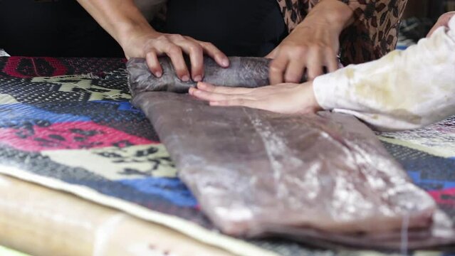 home industry videos. Indonesian women's hands folding a roll of cloth covered in plastic during the process of folding an ecoprint batik cloth.