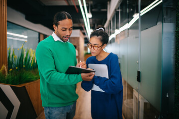 Two colleague creatives talking projects at the office corridor.