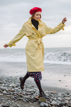 Young woman walking in a yellow raincoat on the coast on a cloudy day