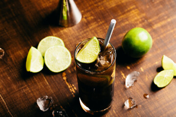 Cuba libre cocktail cold and refreshing drink for summer days on a wooden table with ice and slices of lemons