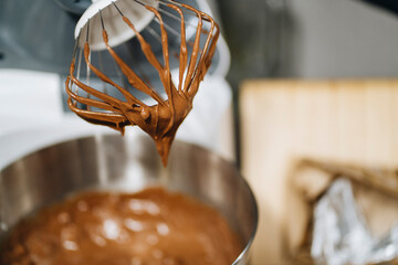 Whisk with chocolate batter in kitchen