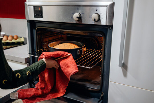 Crop girl taking out hot cake from oven
