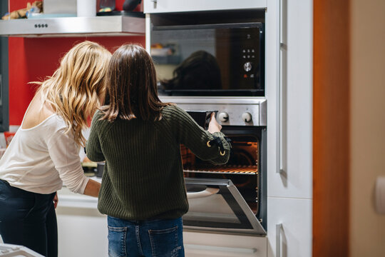 Mom and daughter placing cake in hot oven