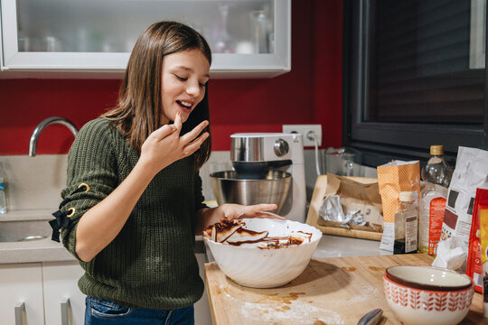 Smiling girl tasting raw chocolate batter from bowl