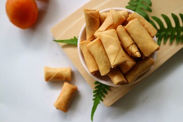 Sumpia or mini crunchy spring rolls on white plate and wooden cutting board. Indonesian homemade crispy fried snack, Wrapped by Kulit Lumpia and filled with Ebi or Shredded Shrimp.
