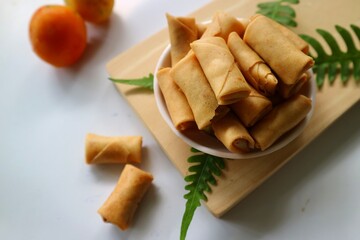 Sumpia or mini crunchy spring rolls on white plate and wooden cutting board. Indonesian homemade crispy fried snack, Wrapped by Kulit Lumpia and filled with Ebi or Shredded Shrimp.