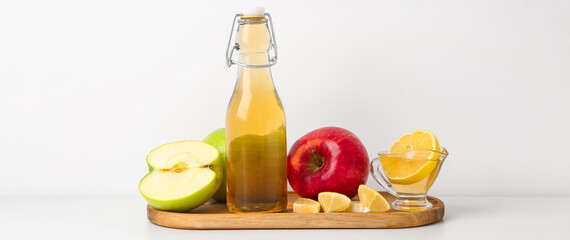 Bottle of apple cider vinegar and fresh fruits on light background