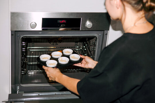 Housewife  put a mold with cupcakes in a preheated oven.