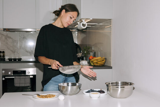 Young woman confectioner sifting flour through a sieve