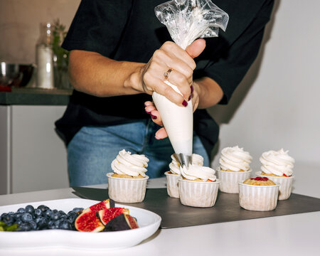 Young woman decorating cupcakes with cream in  pastry sleeve 