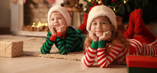 Cute little children in Santa Claus hats and pajamas at home on Christmas eve