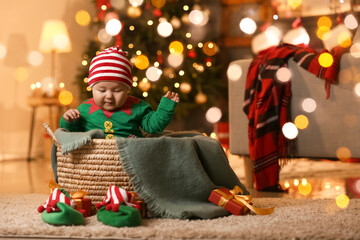 Cute little baby dressed as elf sitting in basket at home on Christmas eve