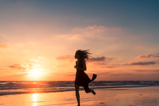 Happy woman enjoying shore run during sunset